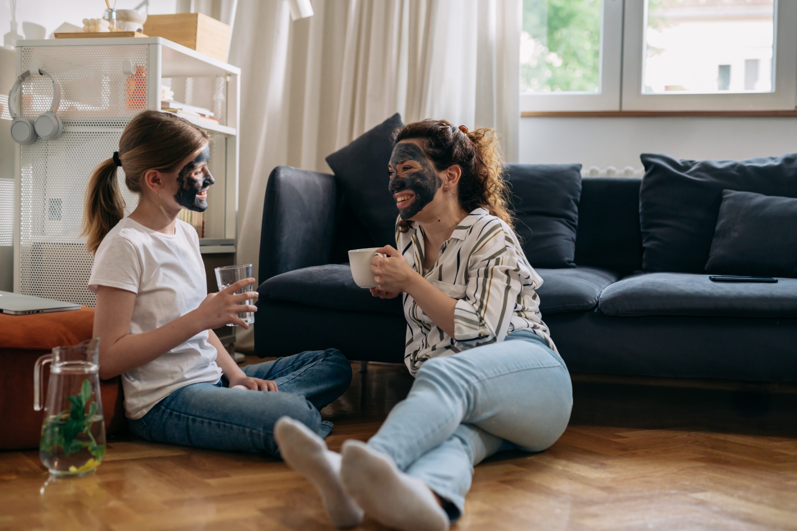 obrazok na webe Kým sa dieťa zobudí - Expresná beauty misia pre mamy Mama a dcéra relaxujú spolu v obývačke, obe majú nanesenú prírodnú pleťovú masku. Mama drží šálku čaju, dcéra pohár vody, a obe sa usmievajú a rozprávajú.